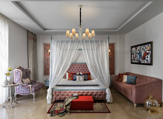 Four-poster canopy bed dressed in white sheer curtains in a grand bedroom with a chandelier and a pink tufted headboard
